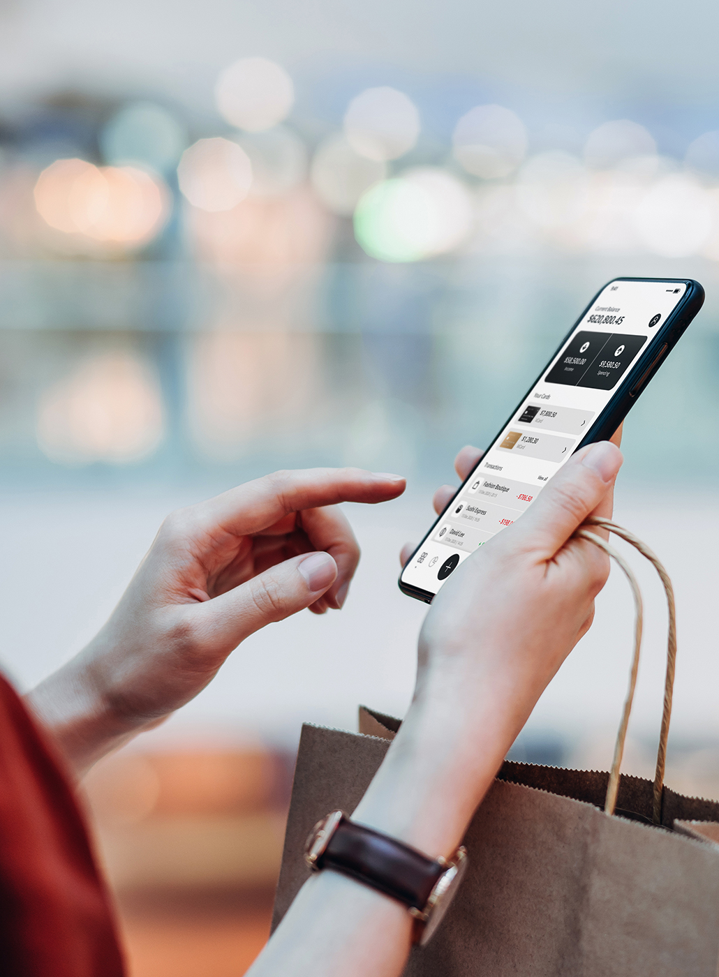 This image shows a woman managing her finances by doing online banking on her phone while shopping in a mall.